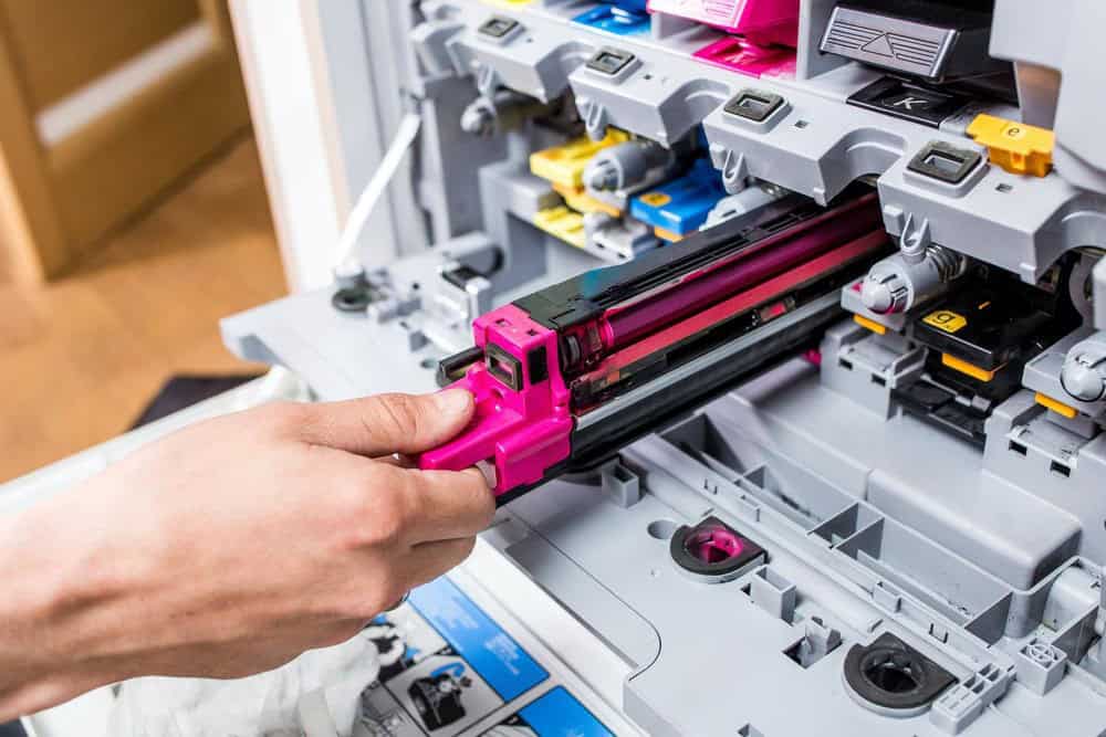 Chegou a hora? Qual é o momento certo de trocar o toner da sua impressora? 16 Mão substituindo o cartucho de toner magenta em uma impressora a laser colorida