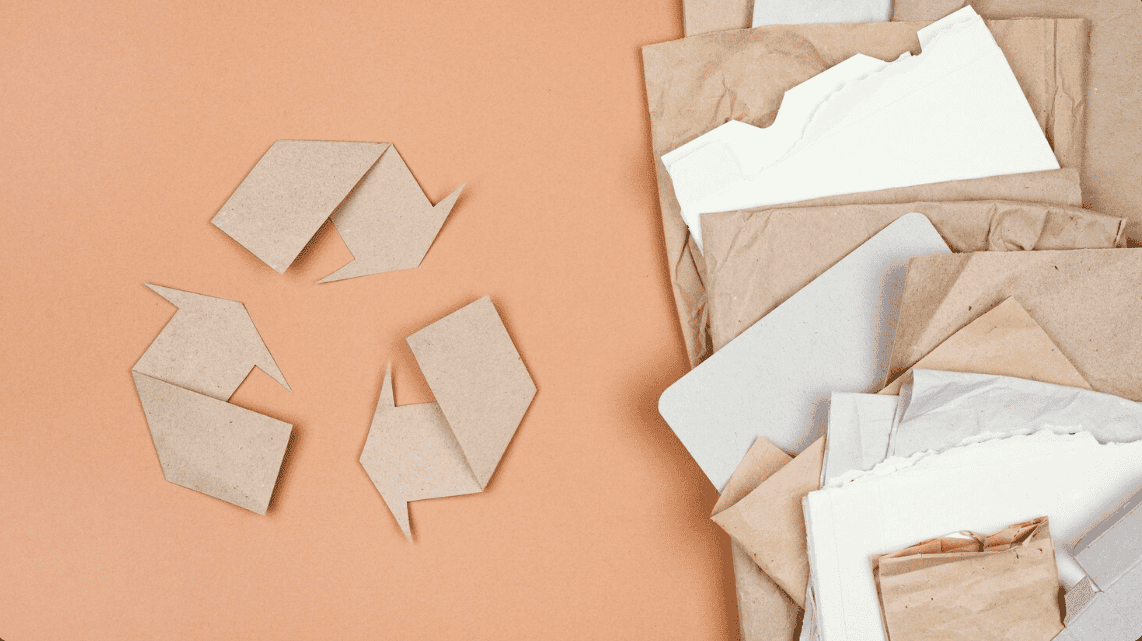 Símbolo de reciclagem em papel kraft ao lado de sacos de papel sobre fundo laranja