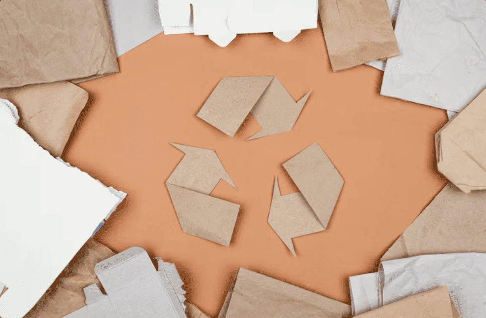 S&iacute;mbolo de reciclagem formado por recortes de papel kraft cercado por sacos de papel