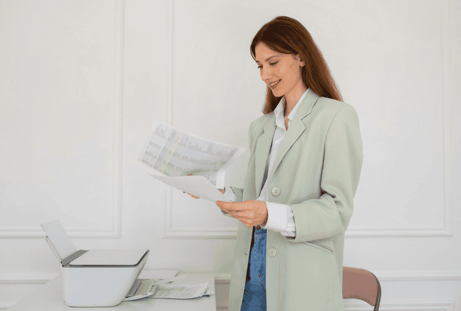 Conheça dicas infalíveis para economizar papel nas empresas! 16 Mulher segurando folhas de papel ao lado de uma impressora