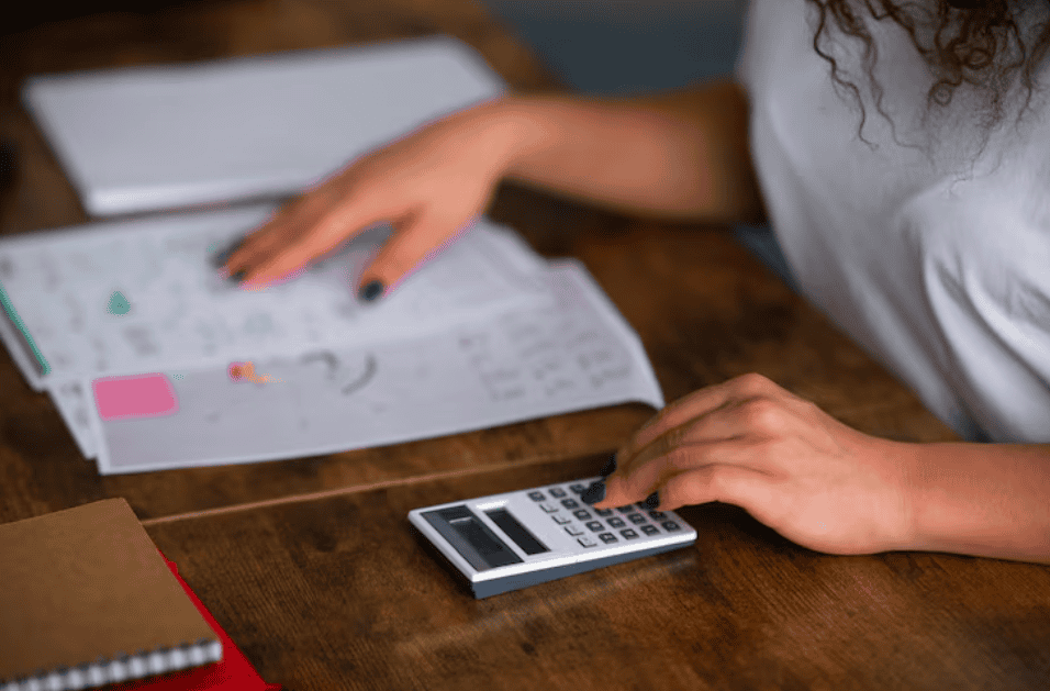 Mulher usando uma calculadora ao lado de documentos e planilhas sobre a mesa