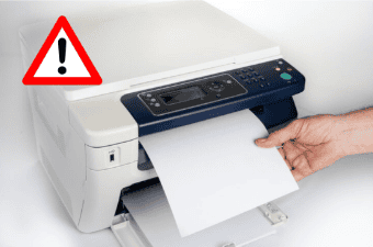 Mão puxando papel preso em uma impressora com símbolo de alerta vermelho