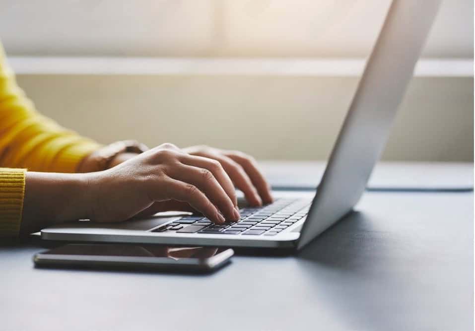 Mãos digitando no teclado de um notebook sobre uma mesa