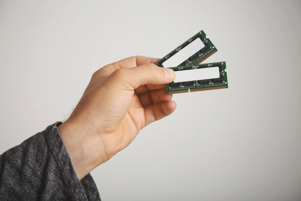 Mão segurando dois pentes de memória RAM para notebook