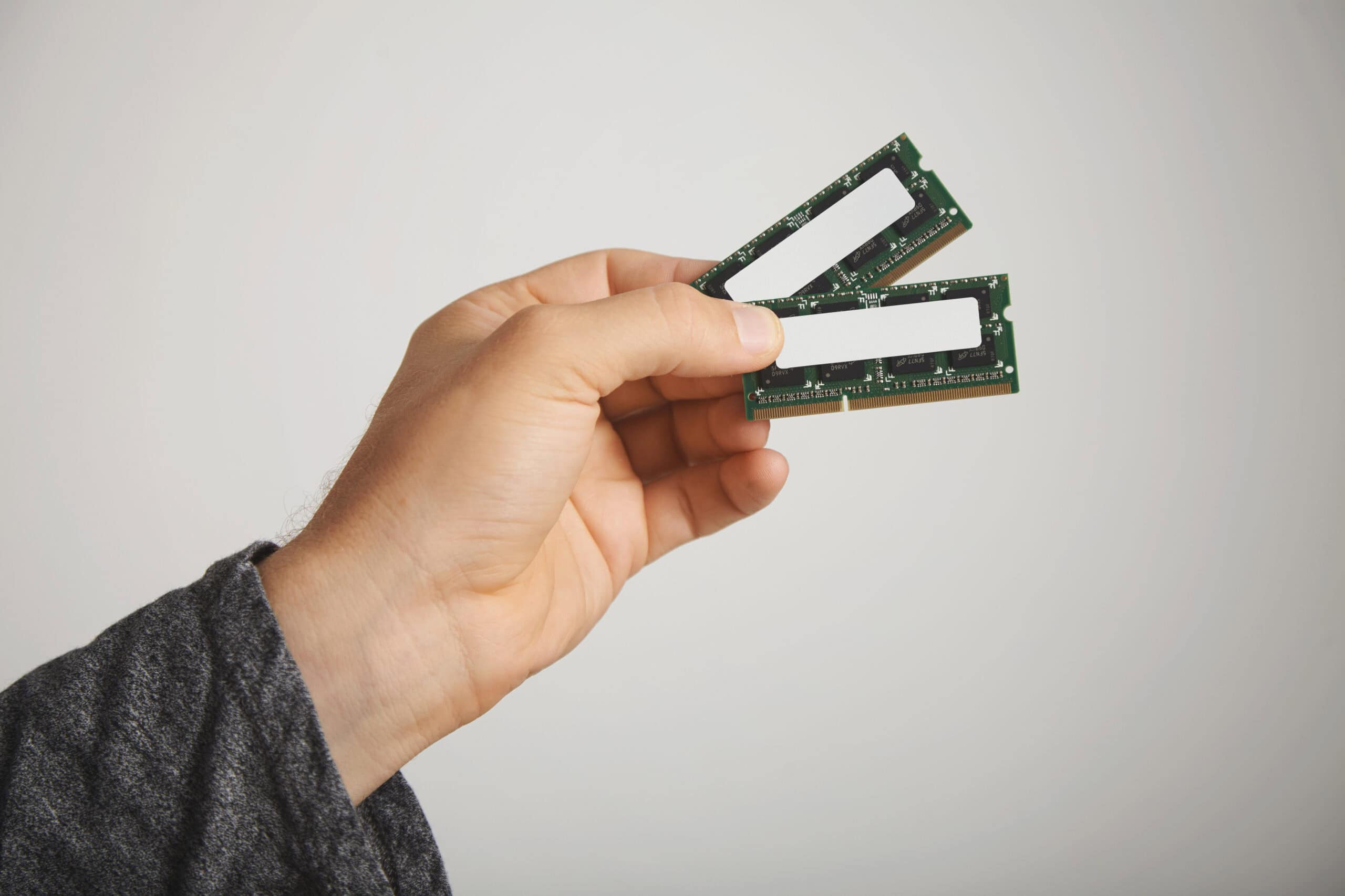 Mão segurando dois pentes de memória RAM para notebook