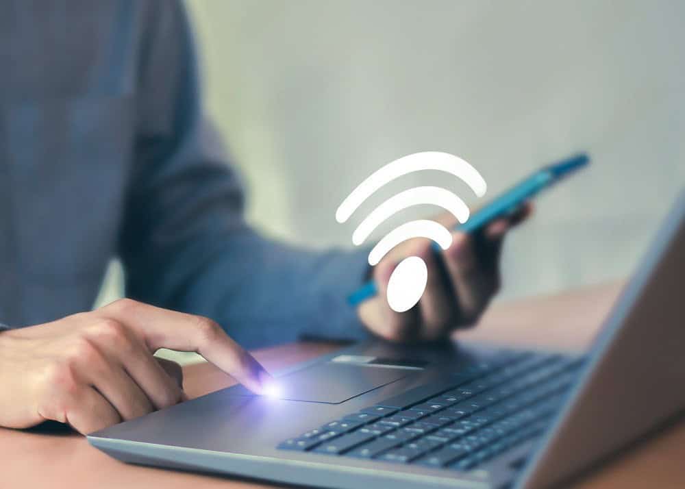 Pessoa usando notebook e celular com símbolo de Wi-Fi em destaque